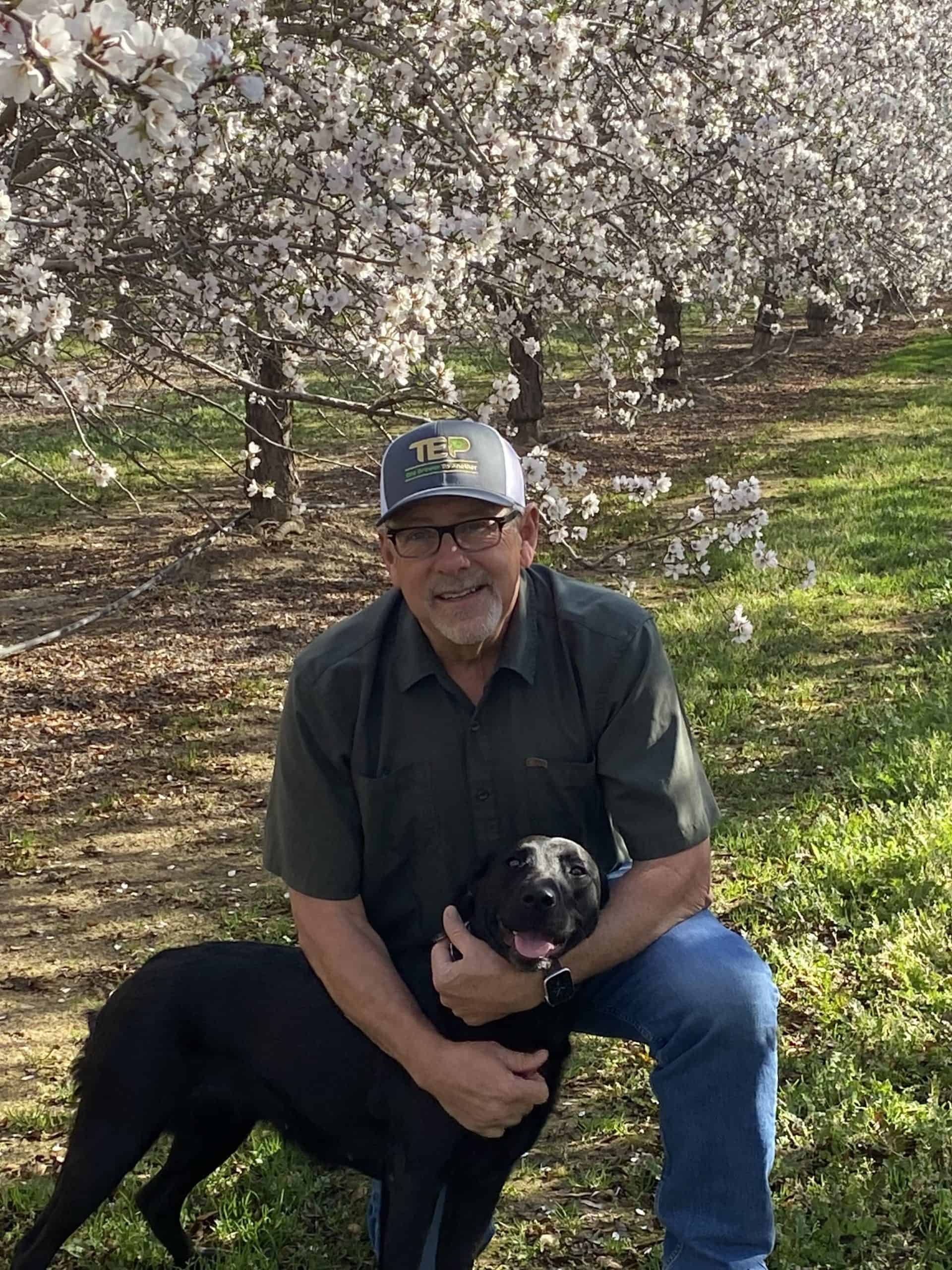  James Pingrey hugs his black dog, Millie, underneath flowering almond trees in an orchard.