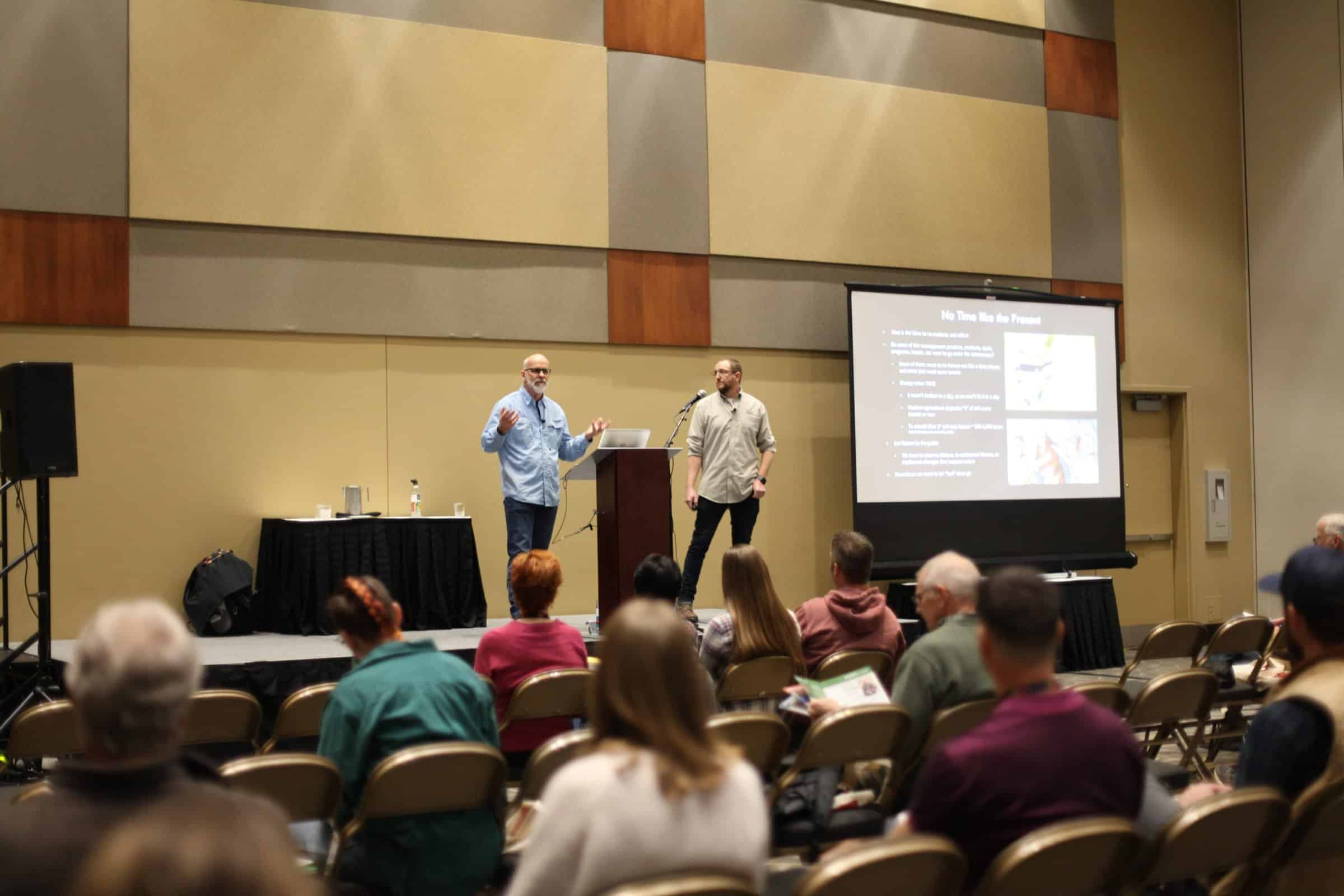 Two presenters on stage in front of a crowd at 2022 Eco-Ag Conference